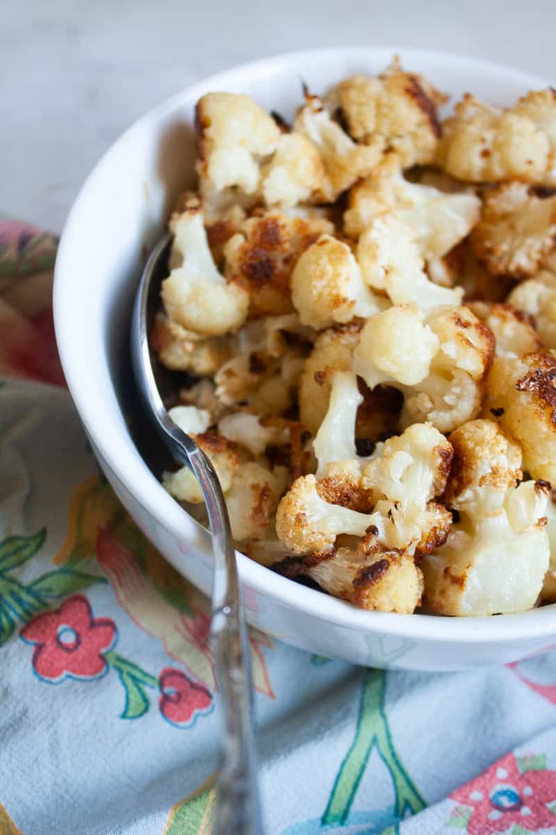 A big bowl of roasted cauliflower with a serving spoon on a blue napkin.