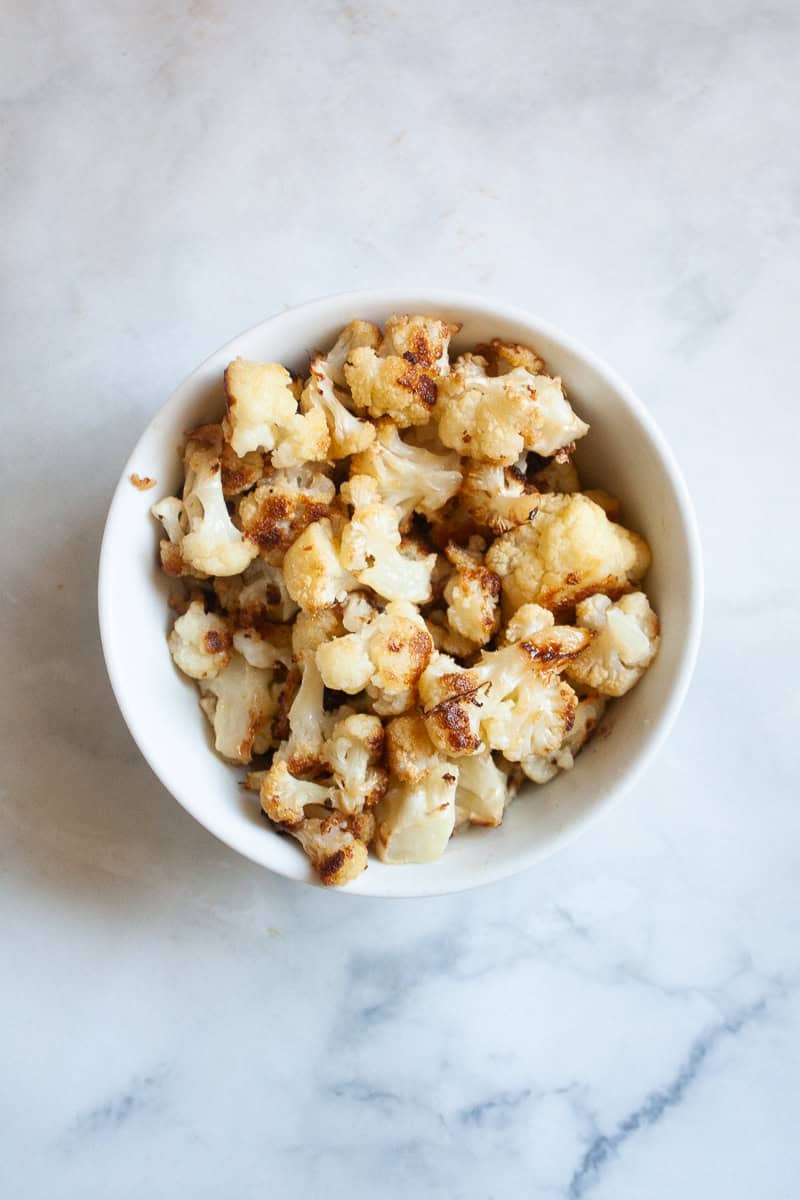 A white bowl of roasted cauliflower on a white background.