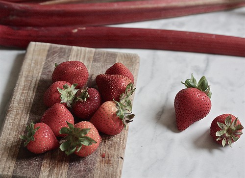 Strawberries and rhubarb on a cutting board.