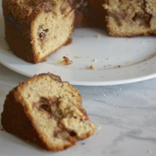 A whole grain apple cake is seen in the background with a slice of cake in the foreground.
