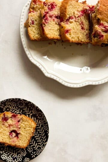 A sliced loaf of lemon cranberry bread and a slice of bread on a plate.