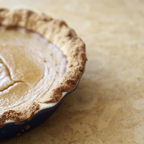 A maple pumpkin pie in a blue pie pan on an orange counter.