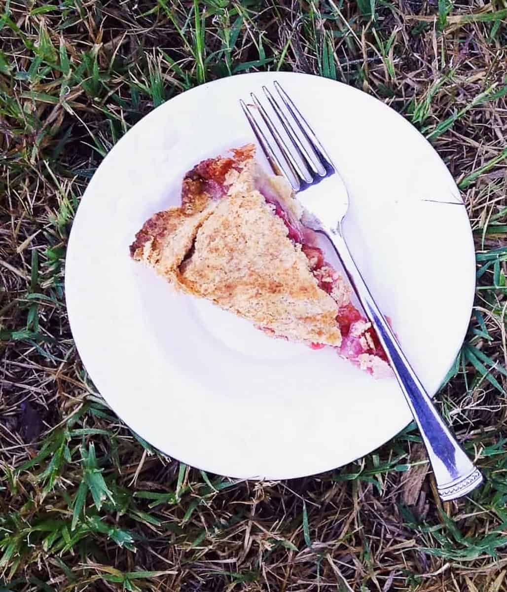 A slice of strawberry rhubarb pie with honey on a white plate with a fork.