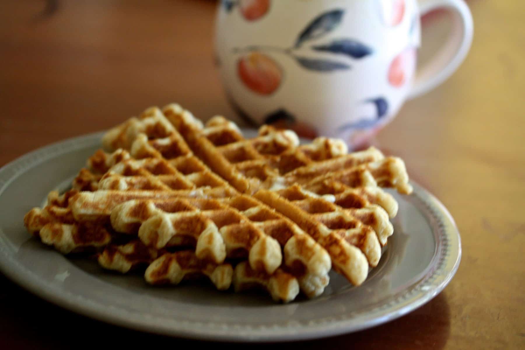 A colorful cup of coffee sits behind a plate of whole grain waffles.