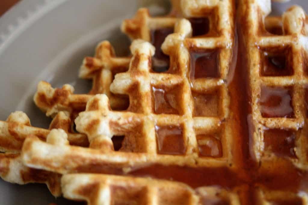 A close up a whole wheat waffle covered in maple syrup.