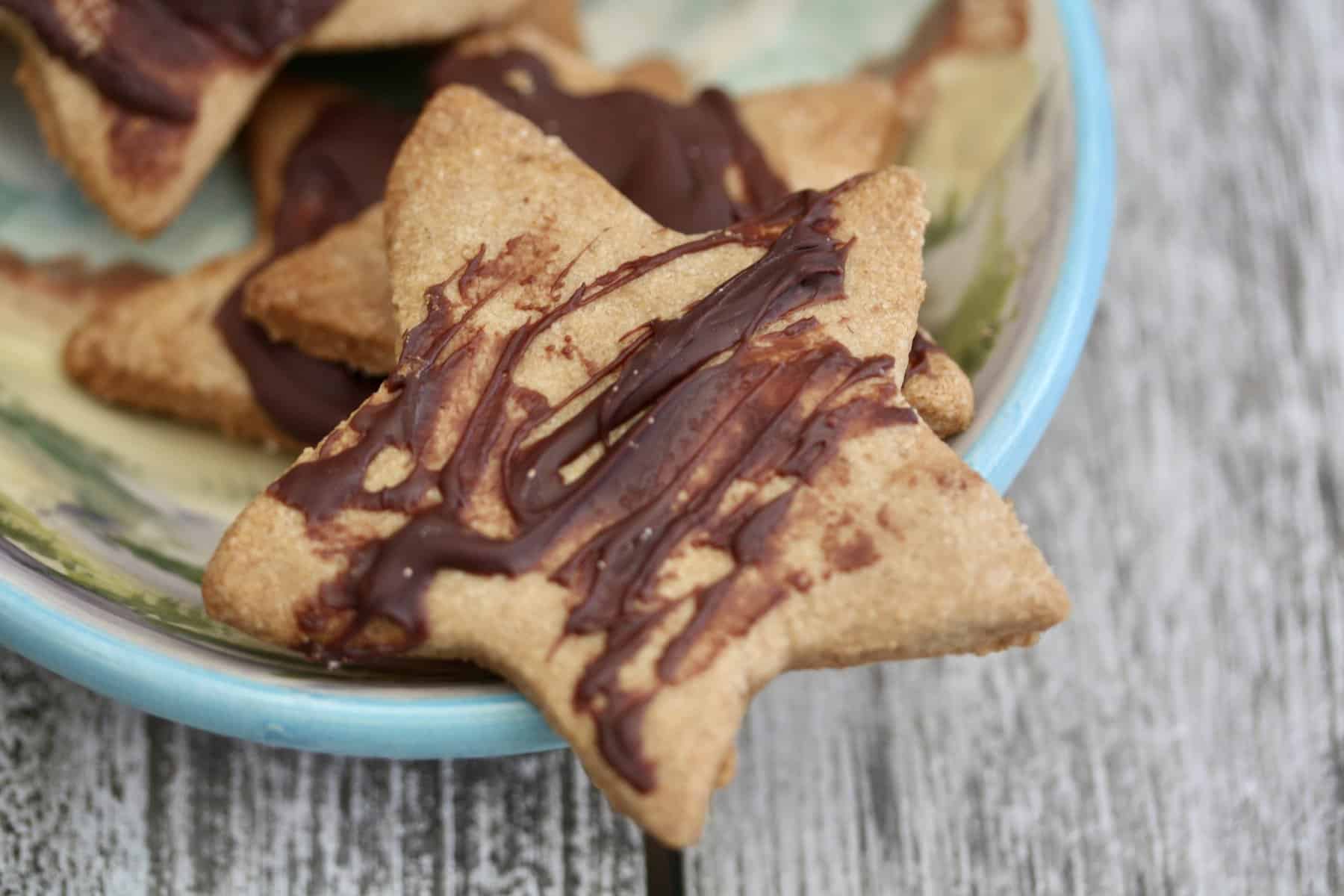 A close up of a dish of gluten free shortbread star cookies drizzled with chocolate.