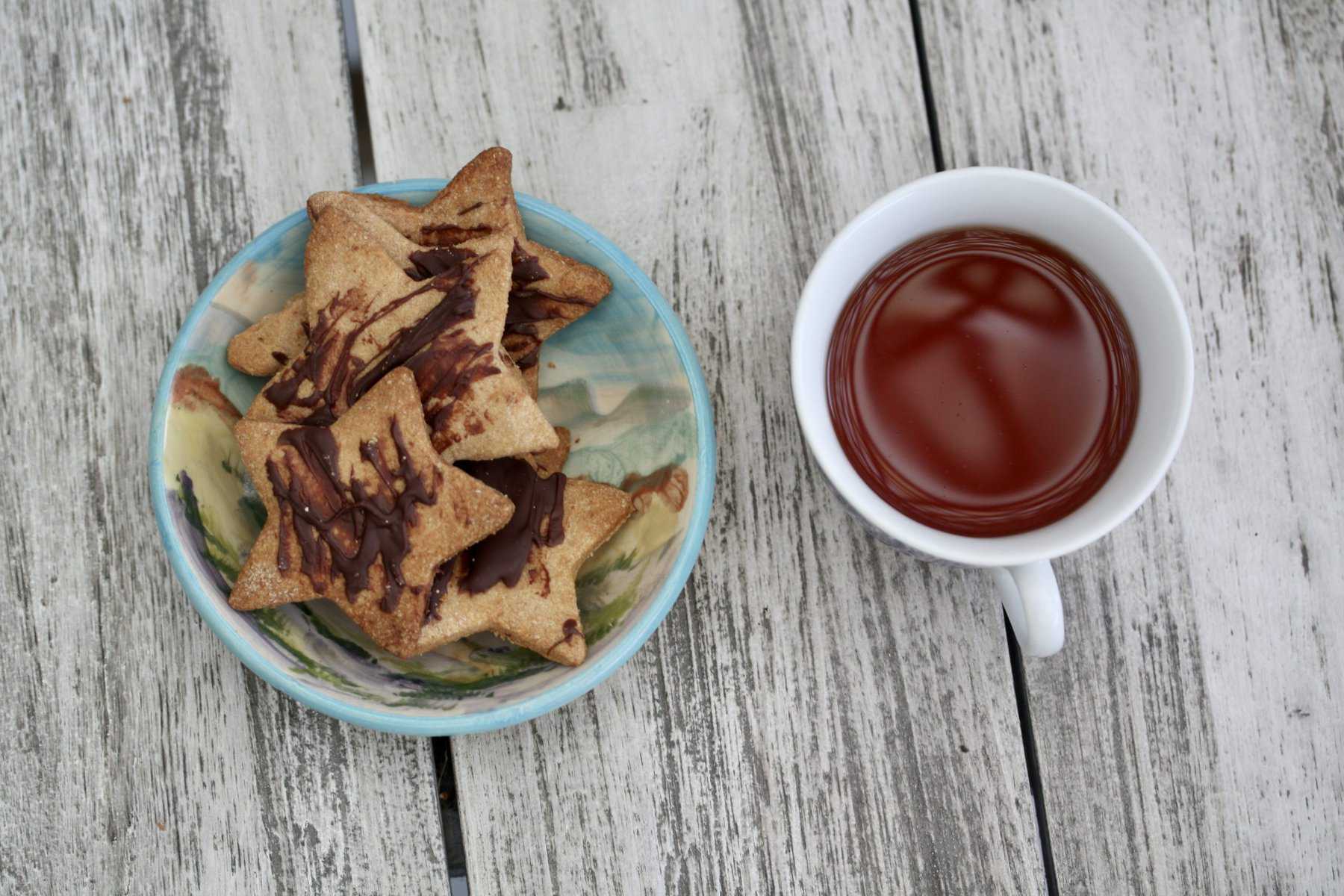 A small bowl of gluten free shortbread star cookies with a cup of tea to its right. 