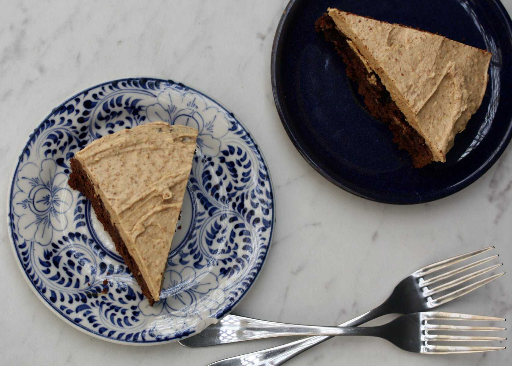 Two slices of gluten-free buttermilk chocolate cake on a white background with two forks.