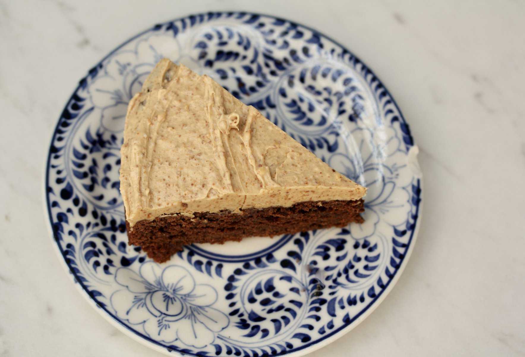 A slice of buttermilk chocolate cake with peanut butter frosting on a blue and white plate.