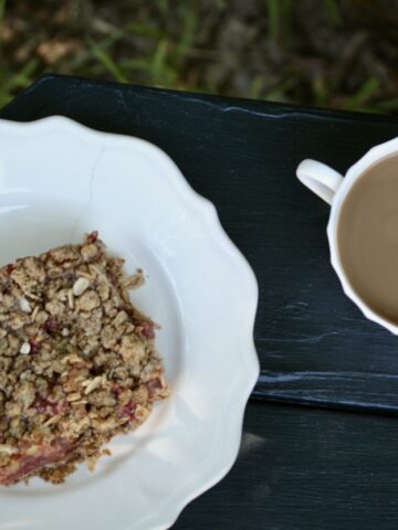 A strawberry rhubarb bar on a plate next to a cup of coffee.