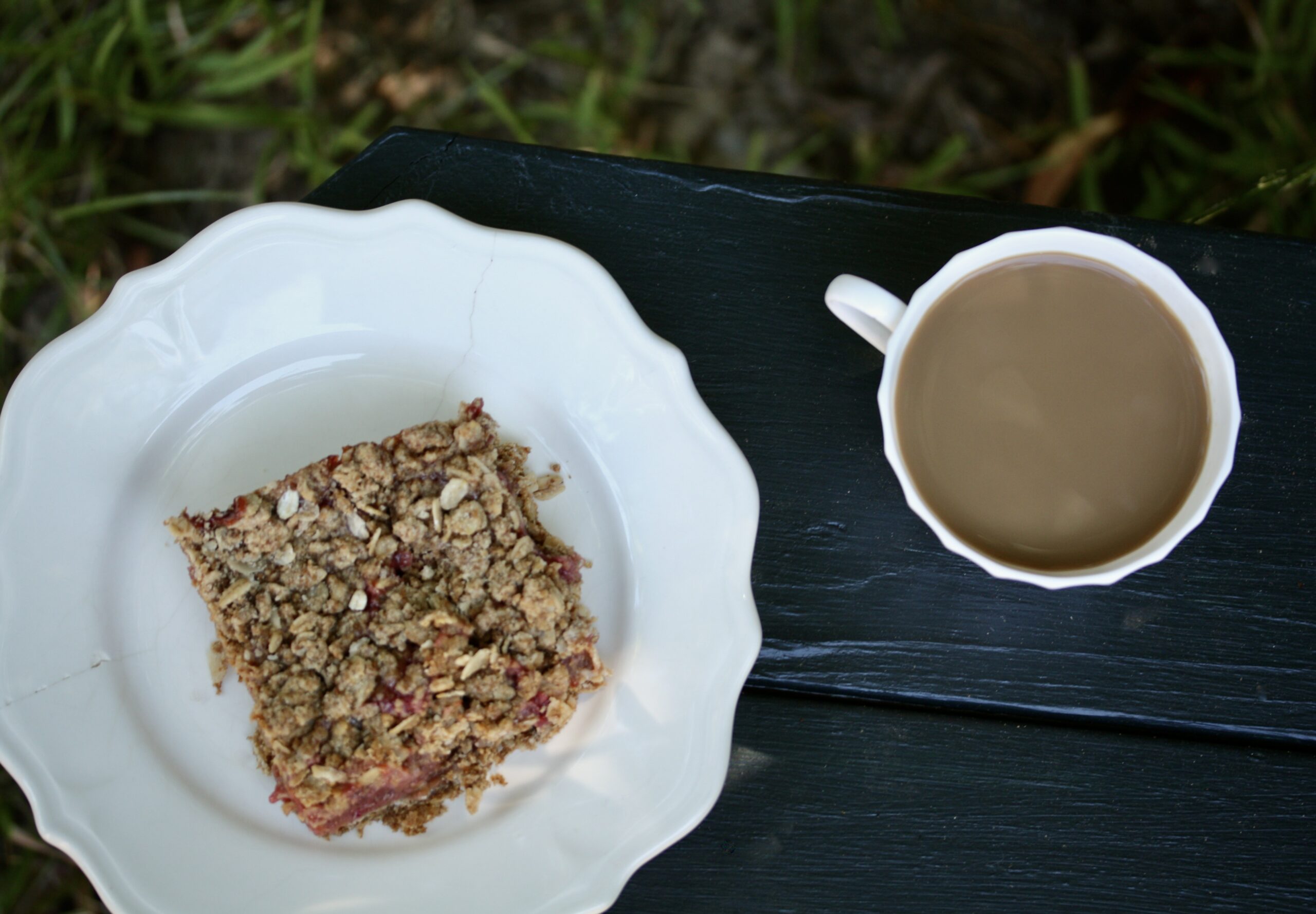 A strawberry rhubarb bar on a plate next to a cup of coffee.