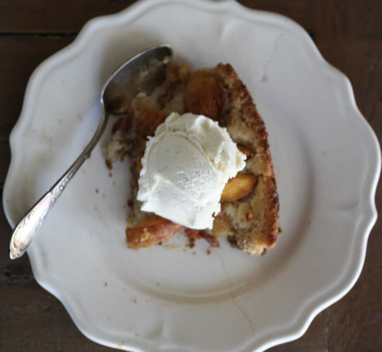 A slice of skillet peach cobbler on a plate topped by vanilla ice cream.