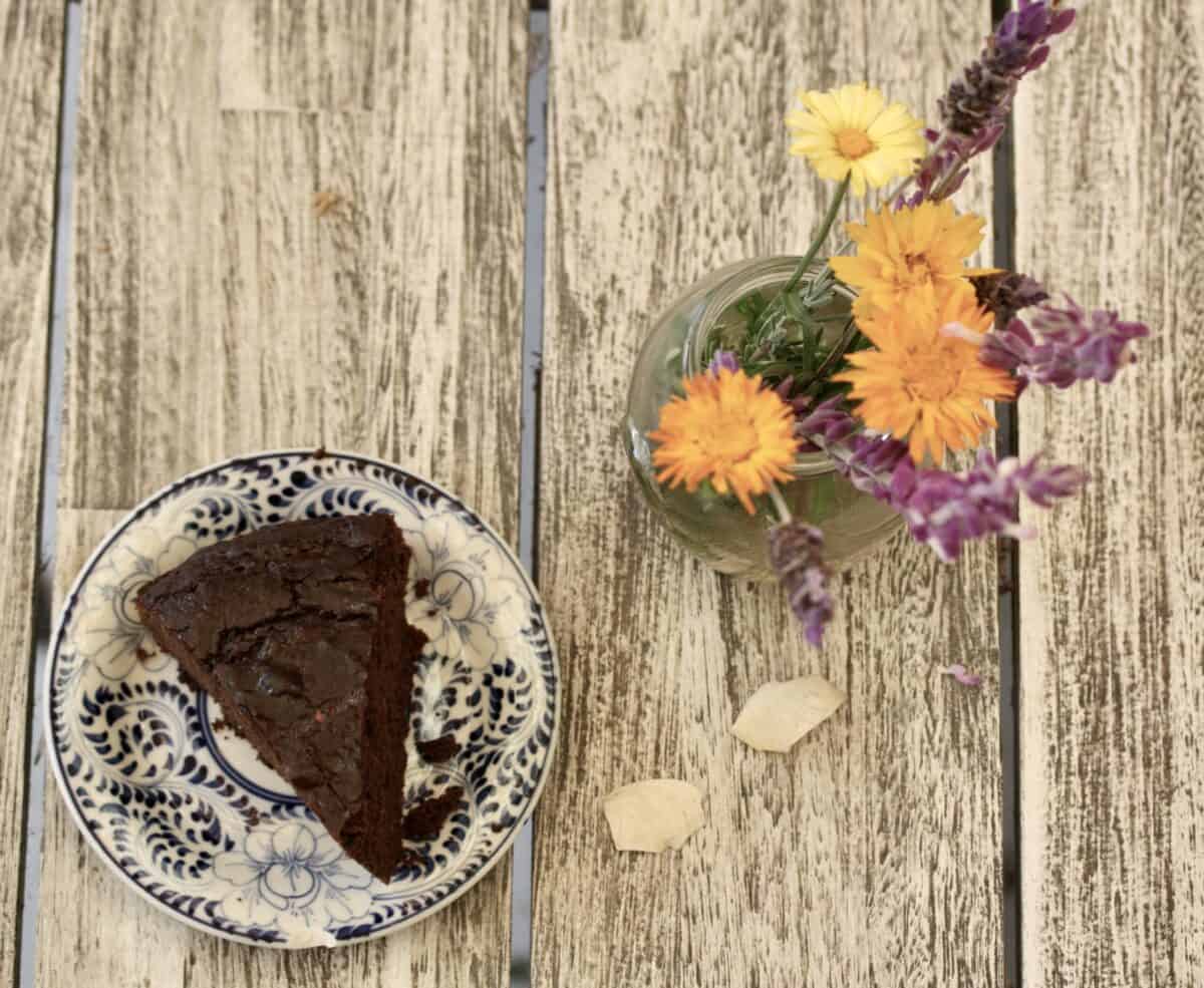 A slice of gluten-free chocolate zucchini cake and flowers on a table.