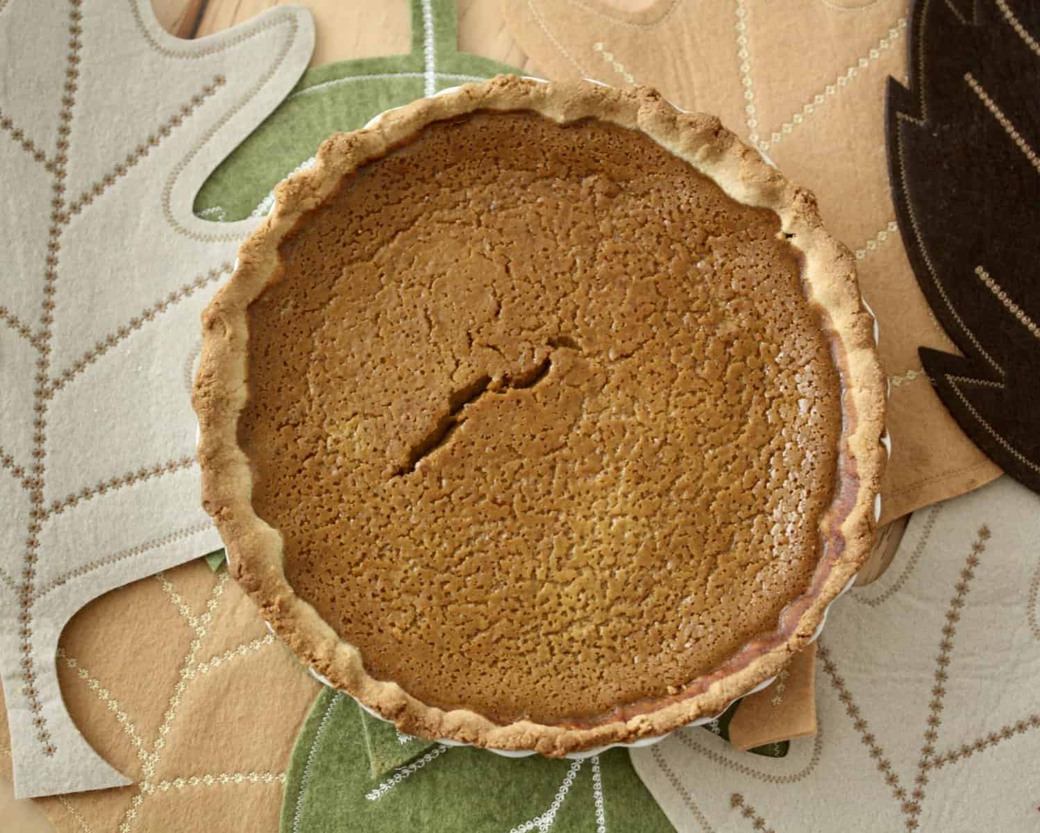 A gluten free pumpkin pie is situated on a leaf table runner.