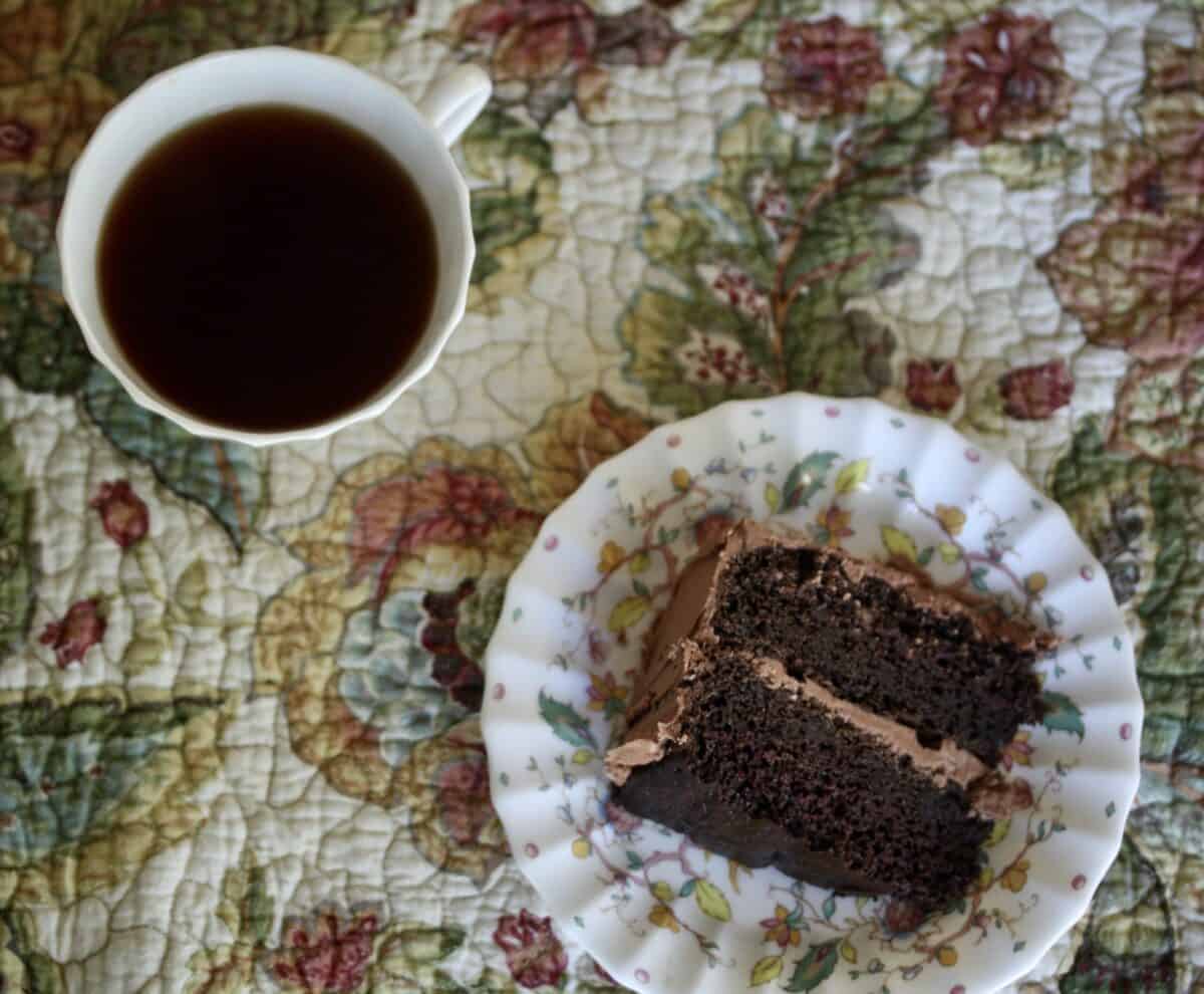 A piece of gluten-free chocolate layer cake and a cup of coffee on a flowered place mat.