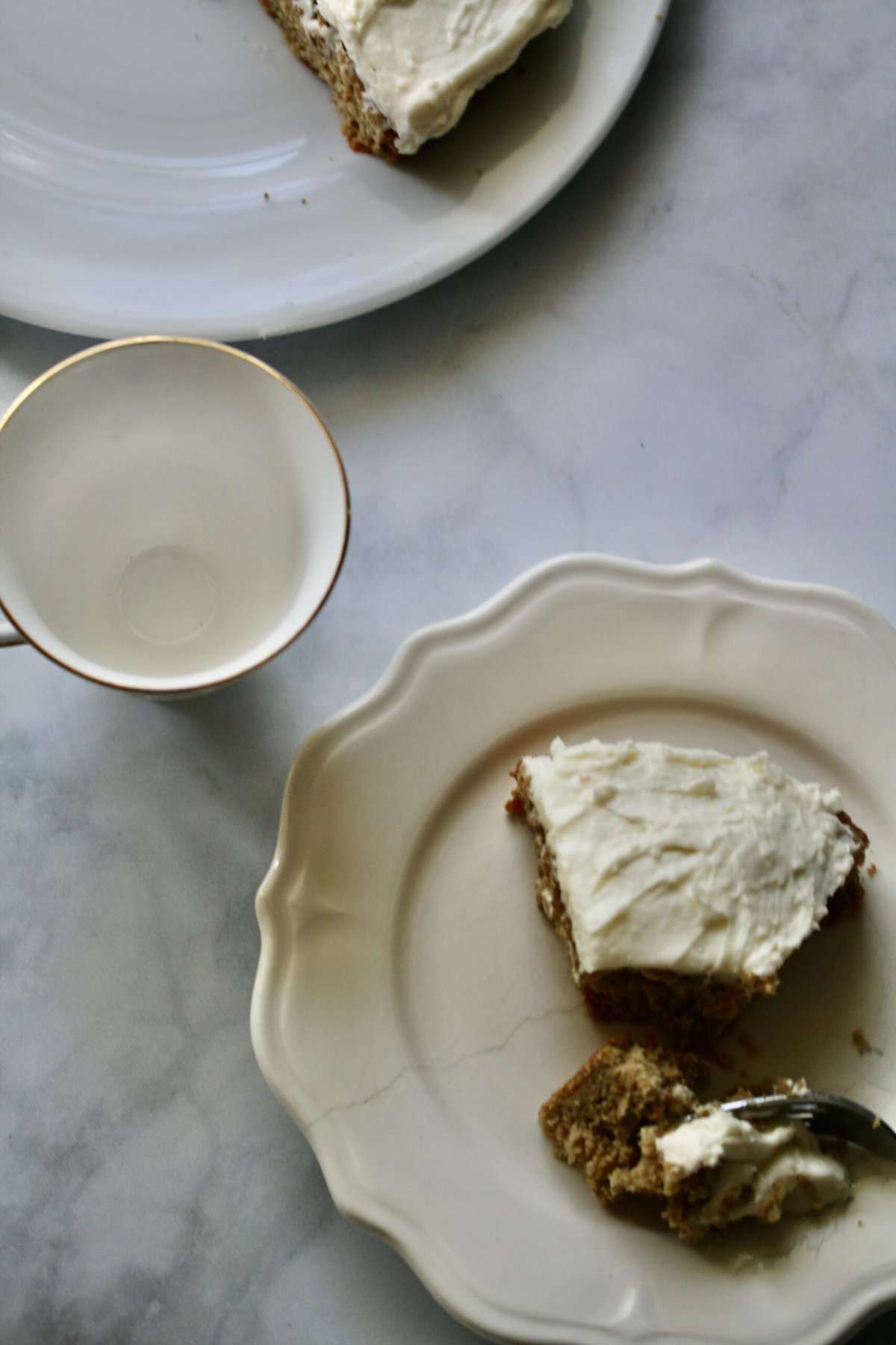 A slice of gluten-free carrot cake on a plate with an empty cup.