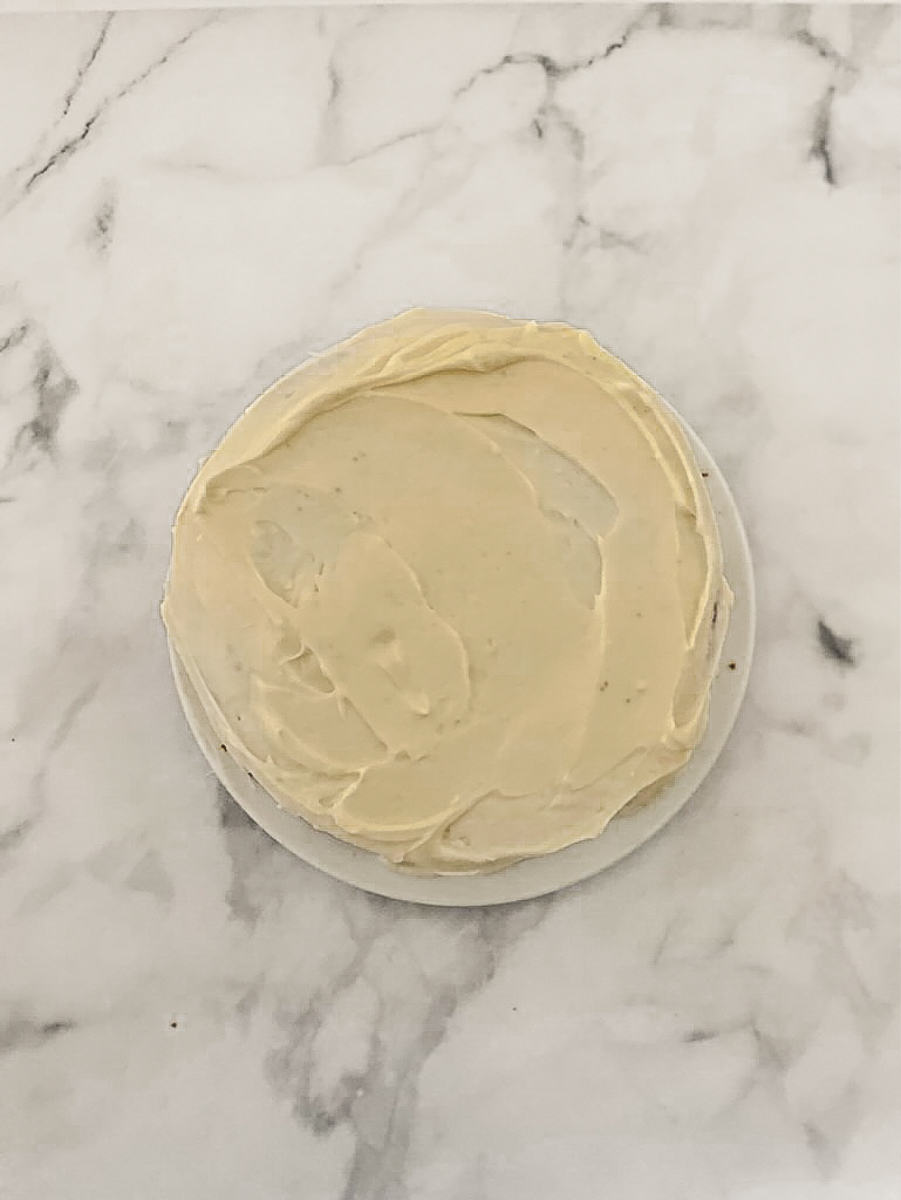A whole banana cake with cream cheese frosting is shown on a white background