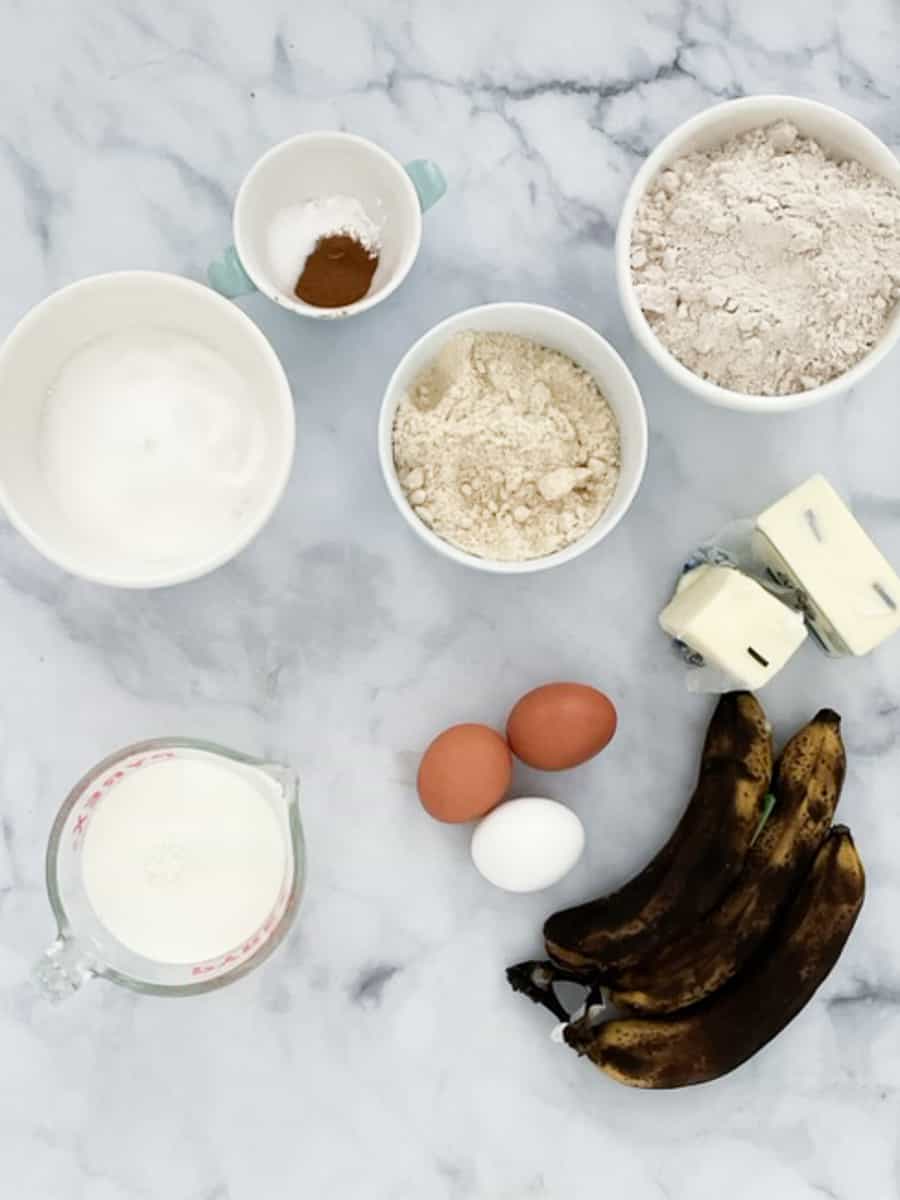 Ingredients for banana cake are shown on a white background - bananas, eggs, gluten free flour, butter