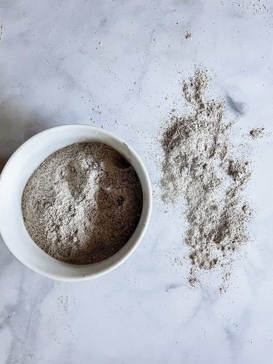 A bowl of buckwheat flour with buckwheat flour next to it on a white background.