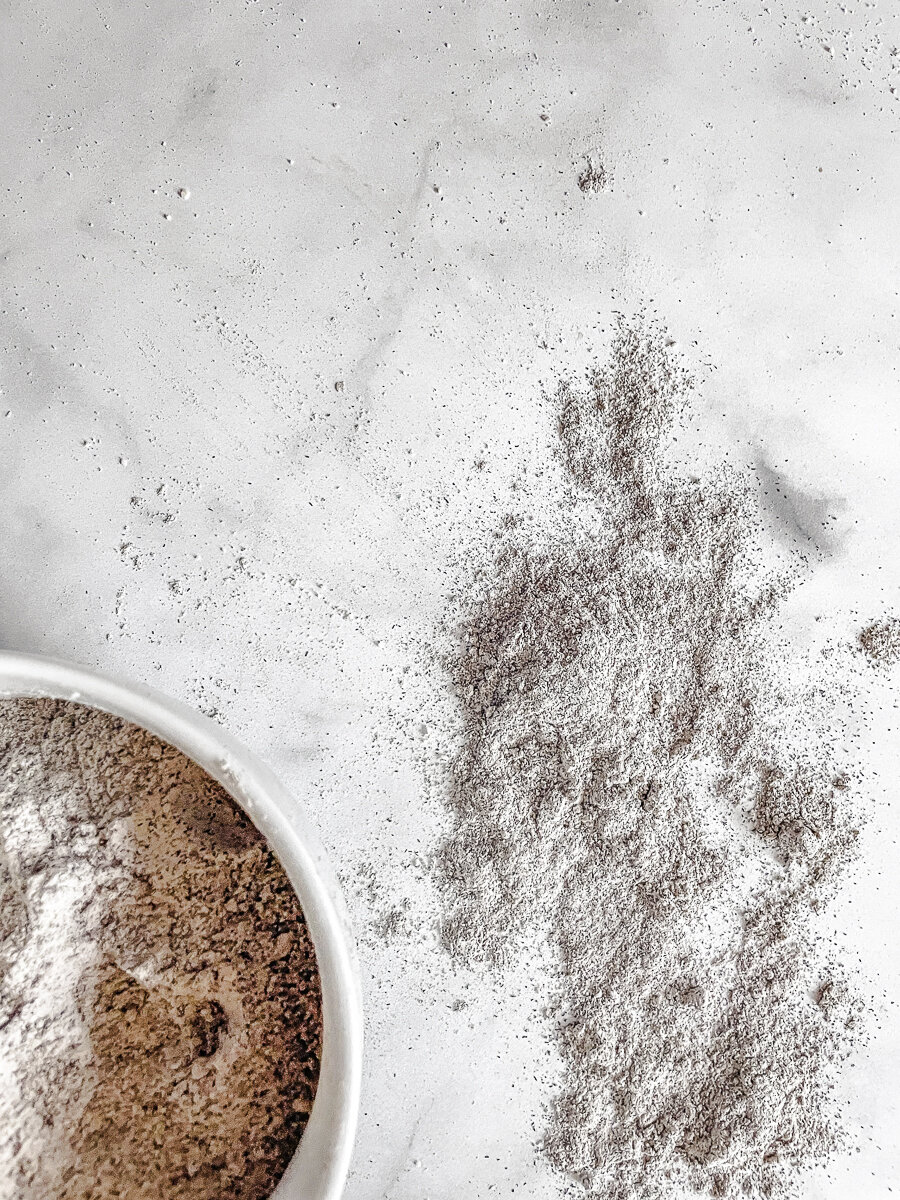 A bowl of buckwheat flour with buckwheat flour next to it on a white background.
