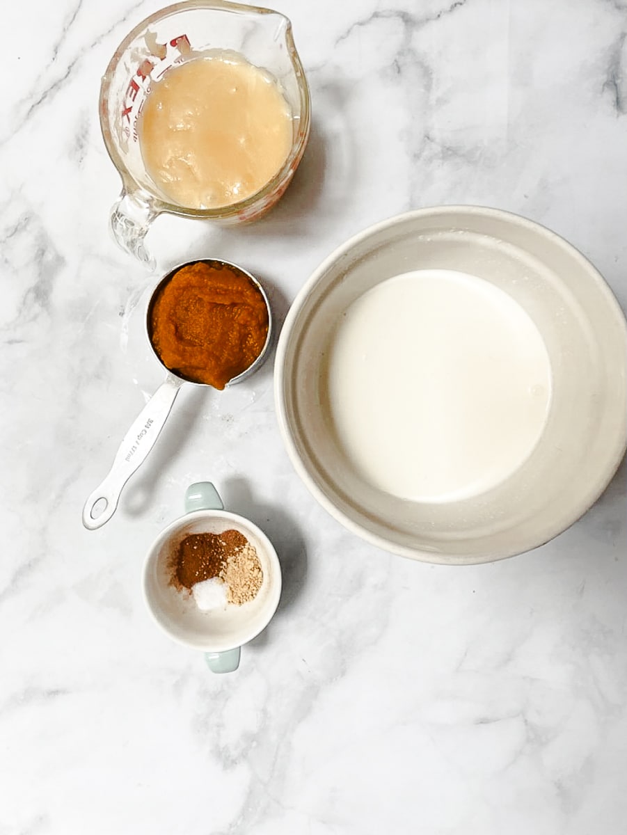 Ingredients for pumpkin ice cream are shown on a white background: condensed milk, pumpkin puree, spices, salt, and heavy cream.