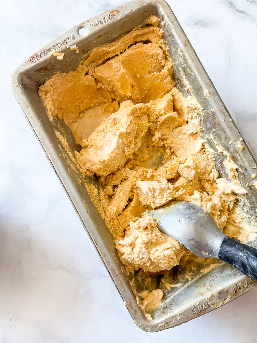 A loaf pan of pumpkin ice cream with an ice cream scoop is shown on a white background.