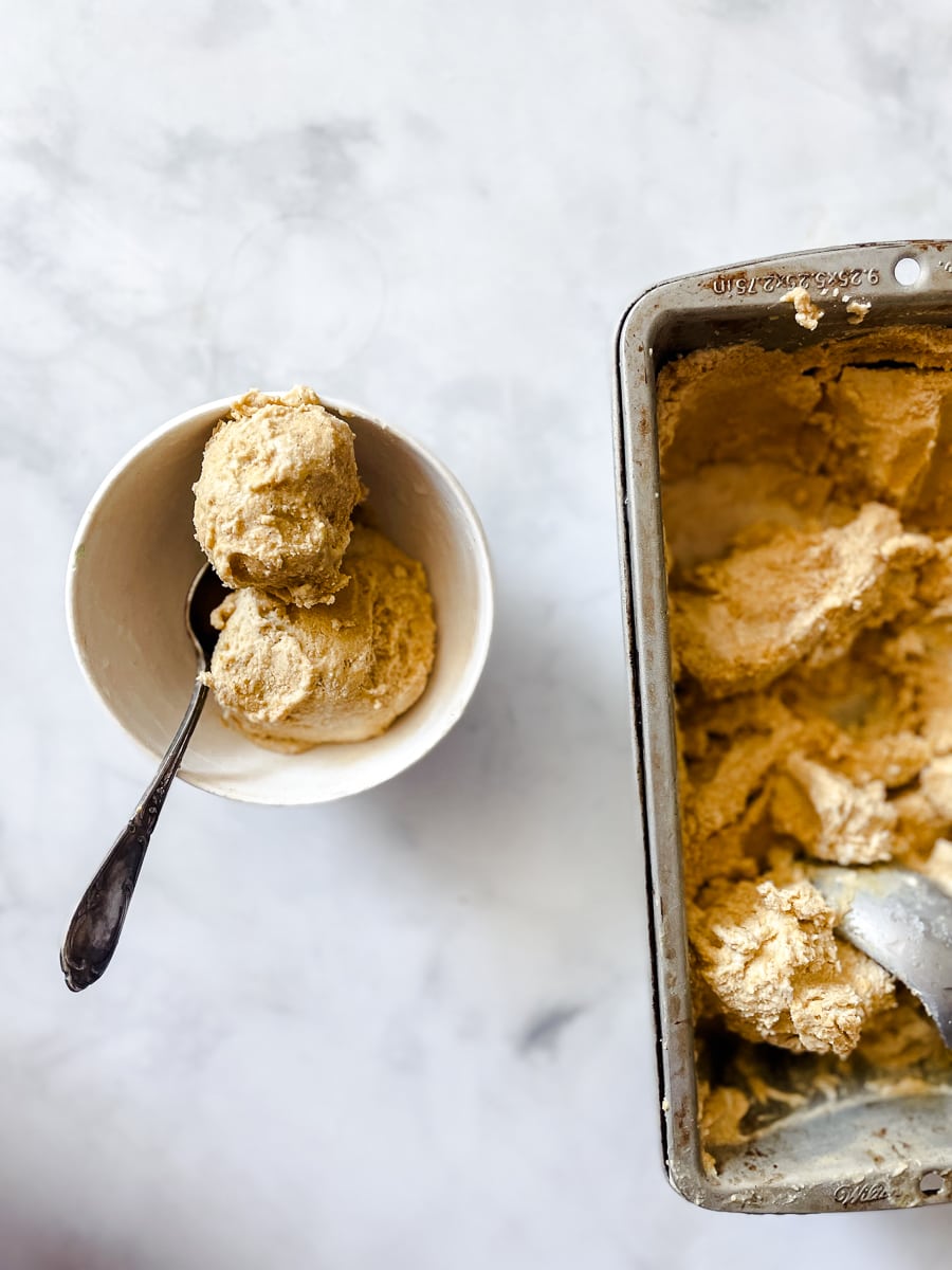 A pan of pumpkin ice cream is shown on a white background with a bowl of pumpkin ice cream next to it.