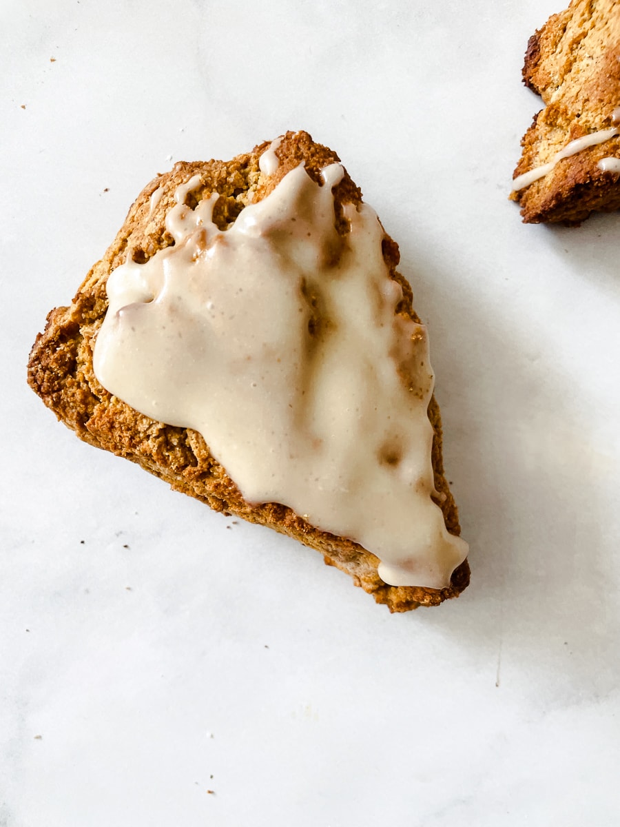 A gluten free pumpkin scone on a white background with glaze.