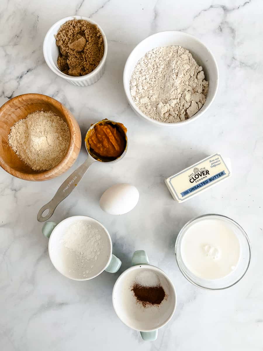 The ingredients needed to make gluten free pumpkin scones are shown portioned out: oat flour, almond flour, baking powder, spices, salt, milk, egg, pumpkin puree, and butter.