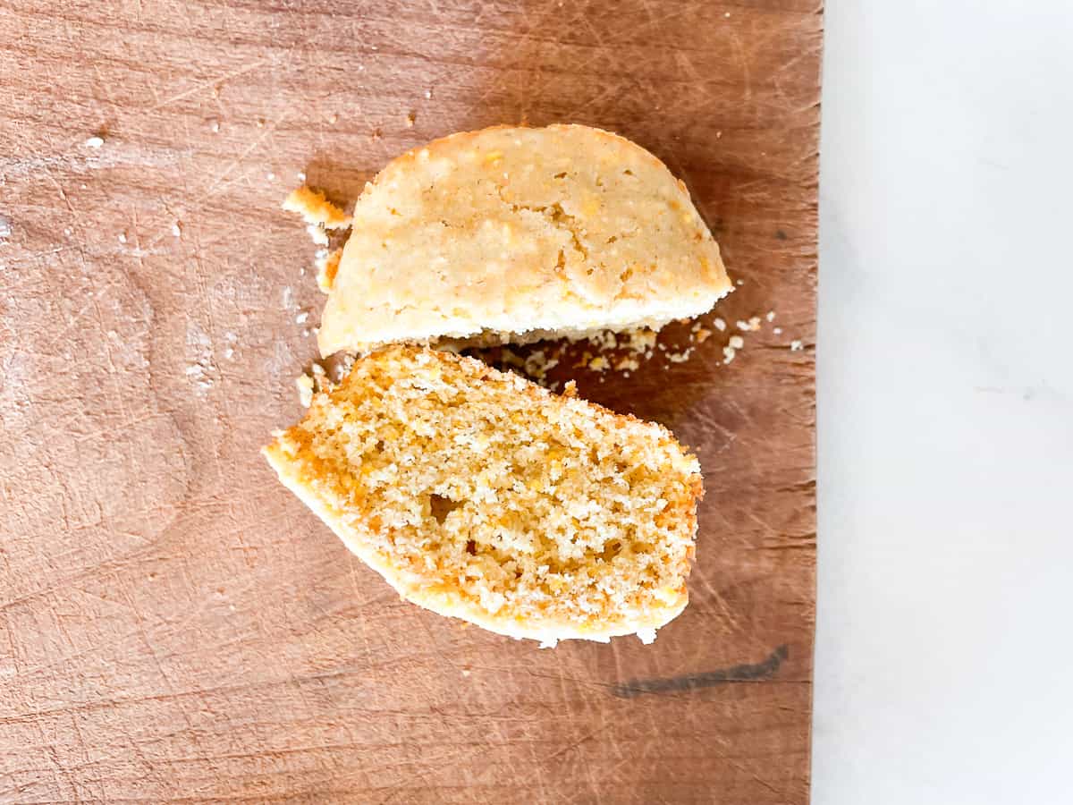 A cut gluten free cornbread muffin on a wooden cutting board.