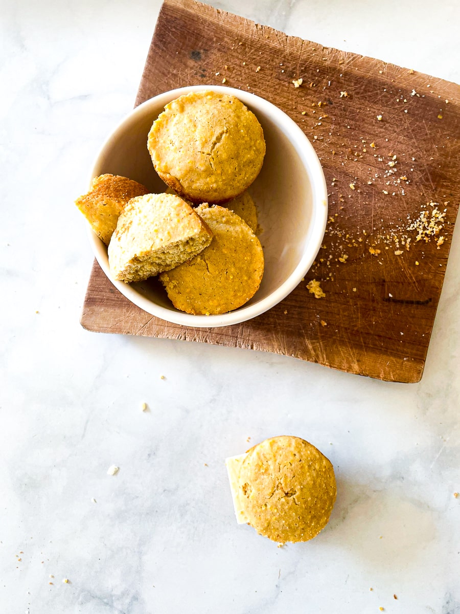 A white bowl of gluten free cornbread muffins on a wooden coating board.