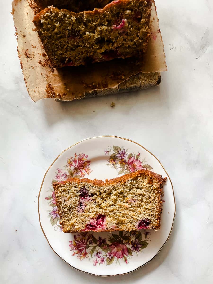 A slice of cranberry orange bread on a floral plate with the loaf nearby.