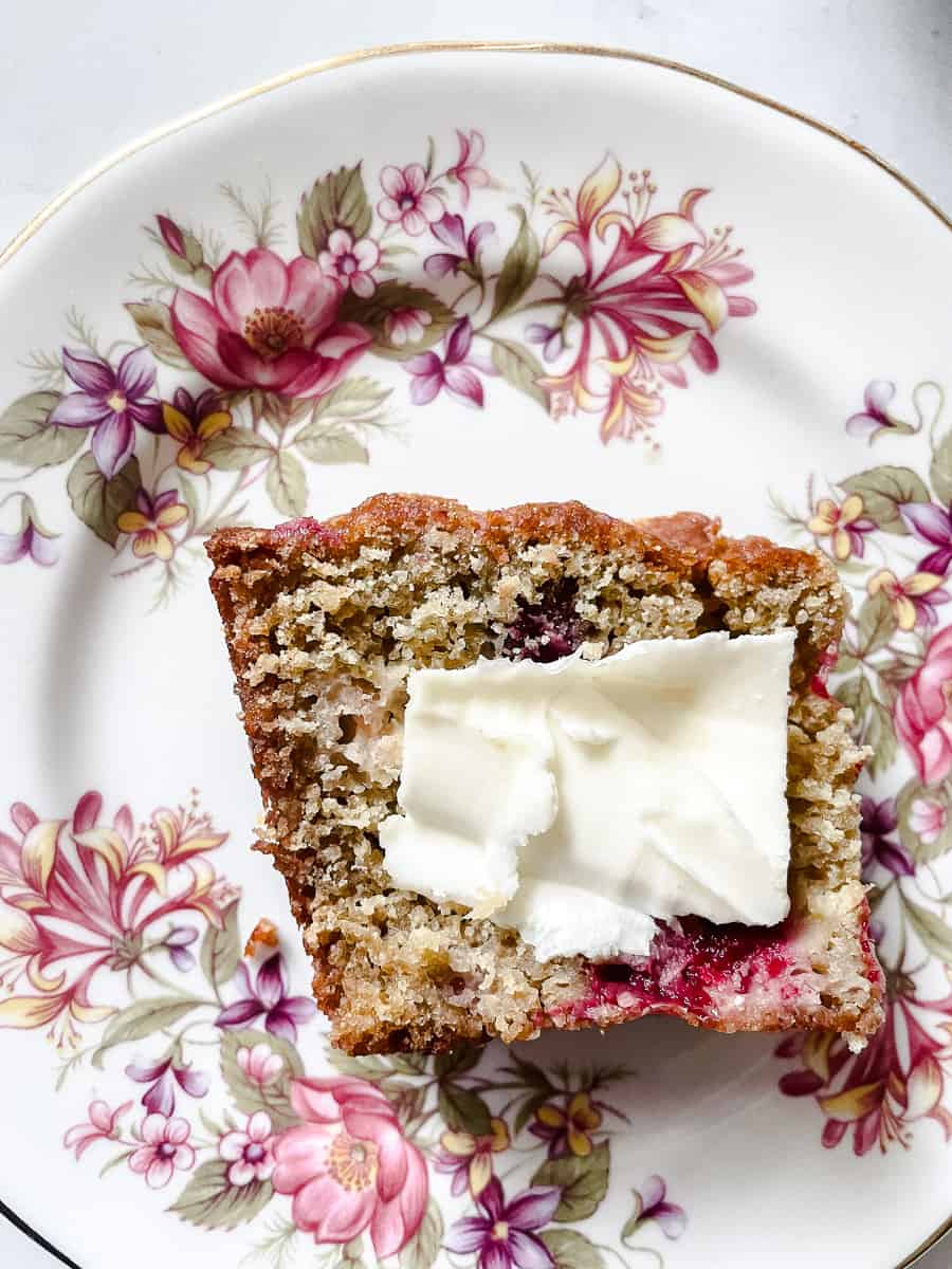 A piece of cranberry orange bread topped with butter on floral plate.