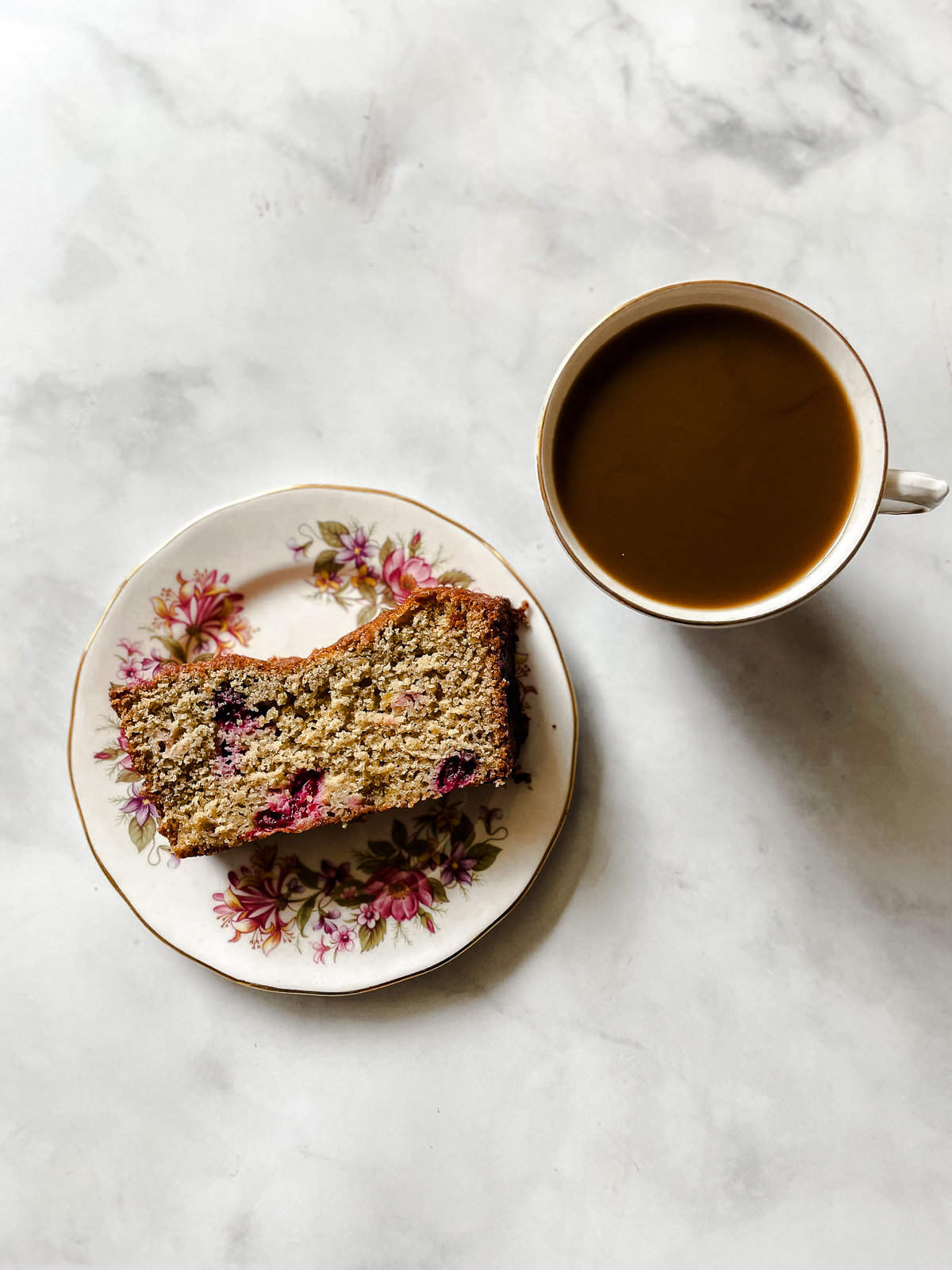 A slice of cranberry orange bread on a plate with a cup of tea.