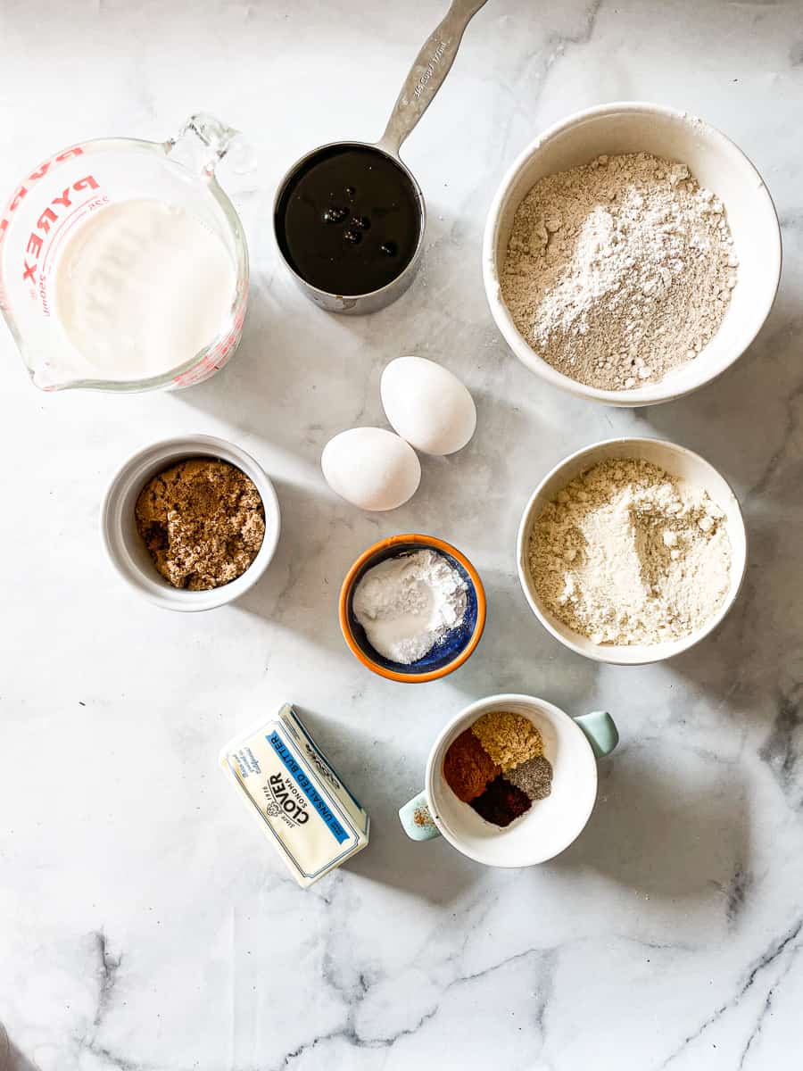 The ingredients needed for gluten free gingerbread are shown portioned out: oat flour, almond flour, buttermilk, butter, molasses, brown sugar, eggs, spices.