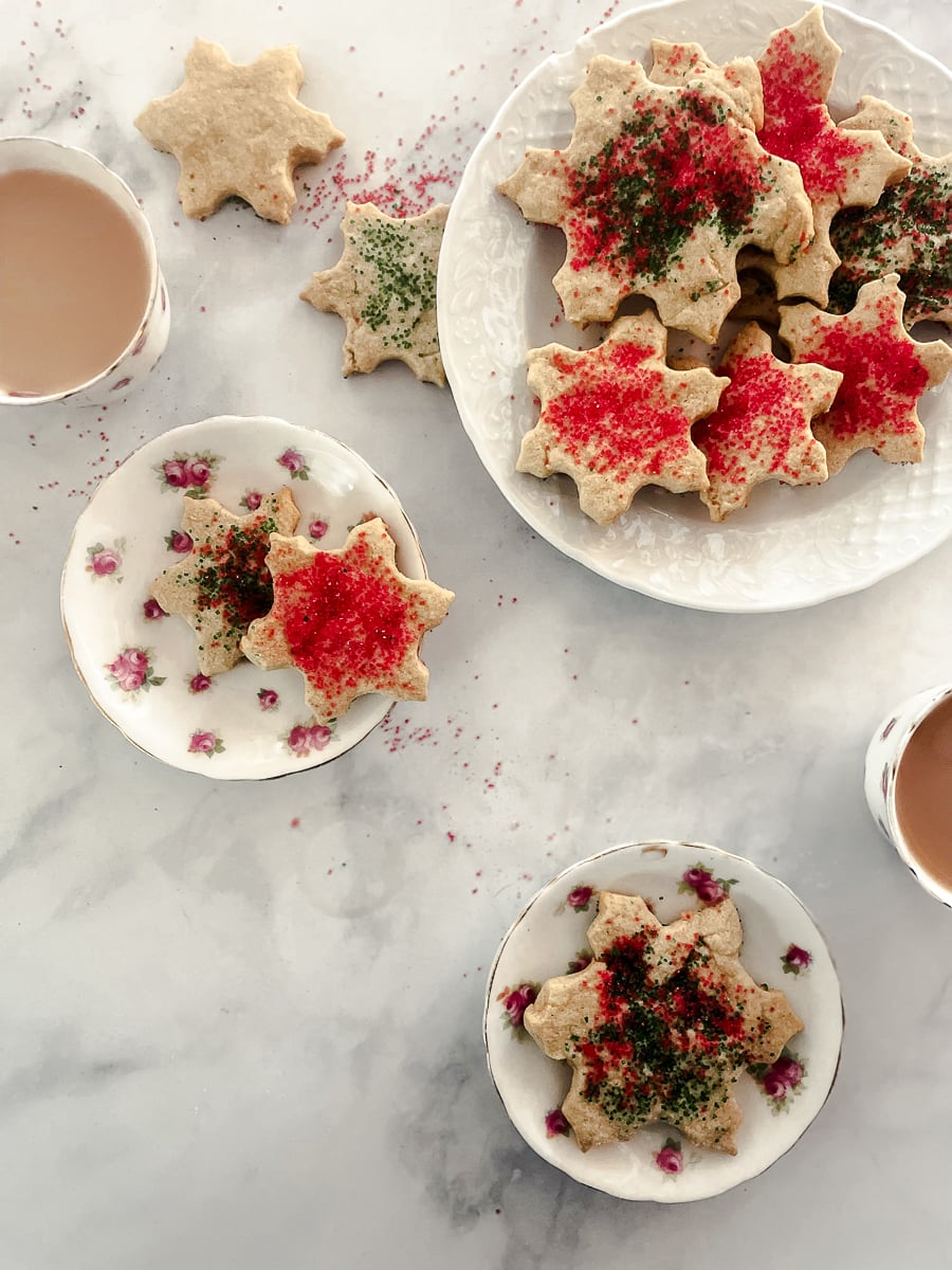 A plate of oat flour sugar cookies is surrounded by more plates of cookies and cups of tea.