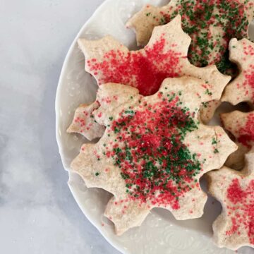 A side view of a plate of red and green sprinkle-topped oat flour sugar cookies.