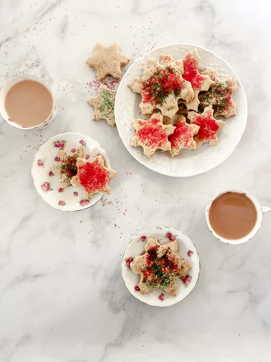 A plate of oat flour sugar cookies topped with sprinkles on a plate with two cups of tea and two small plates of cookies.