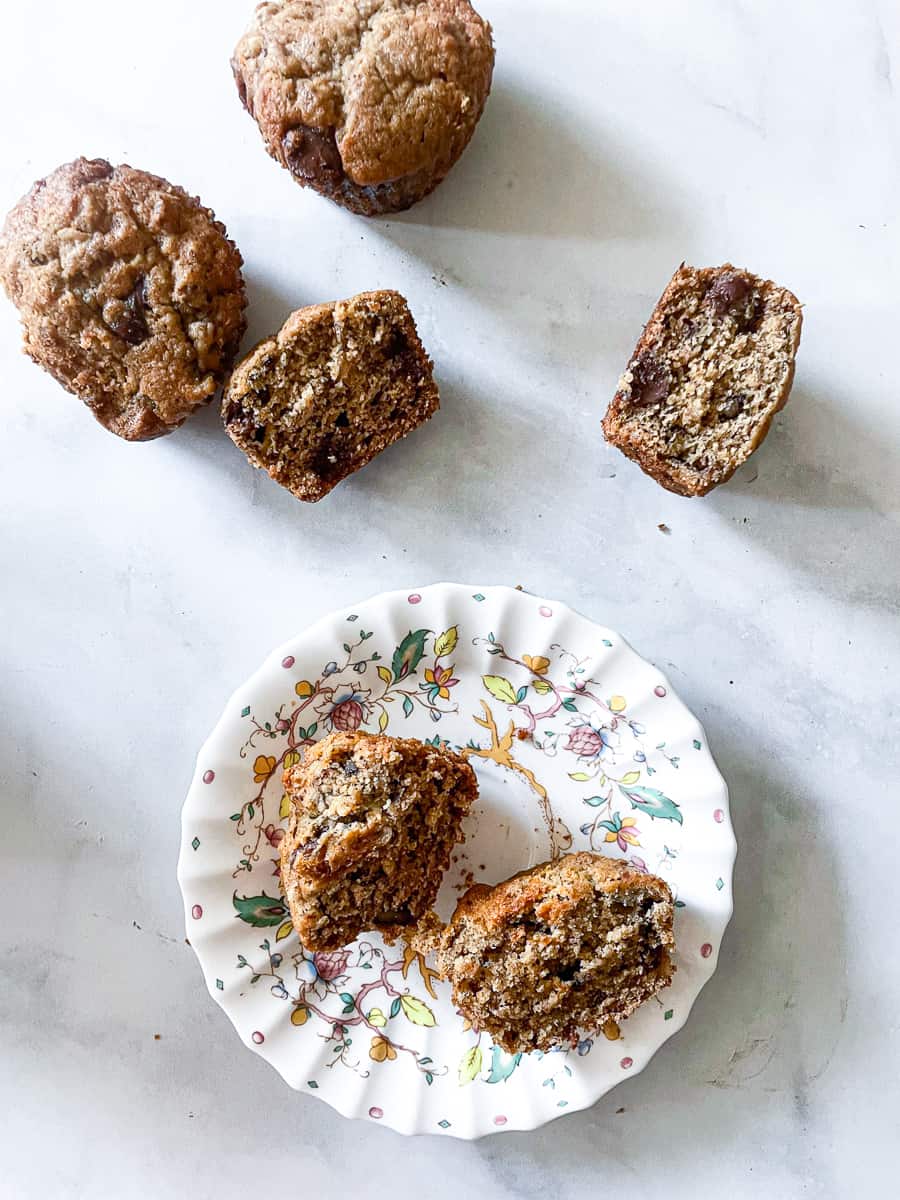 Oat flour banana muffins are scattered on a white background with a muffin on a plate.