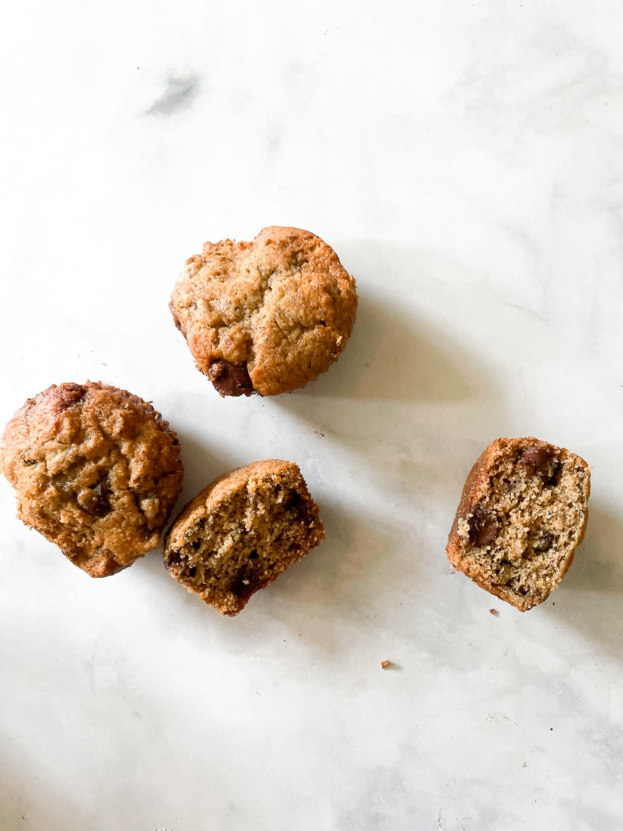 Oat flour banana muffins on a white background with one cut in half.