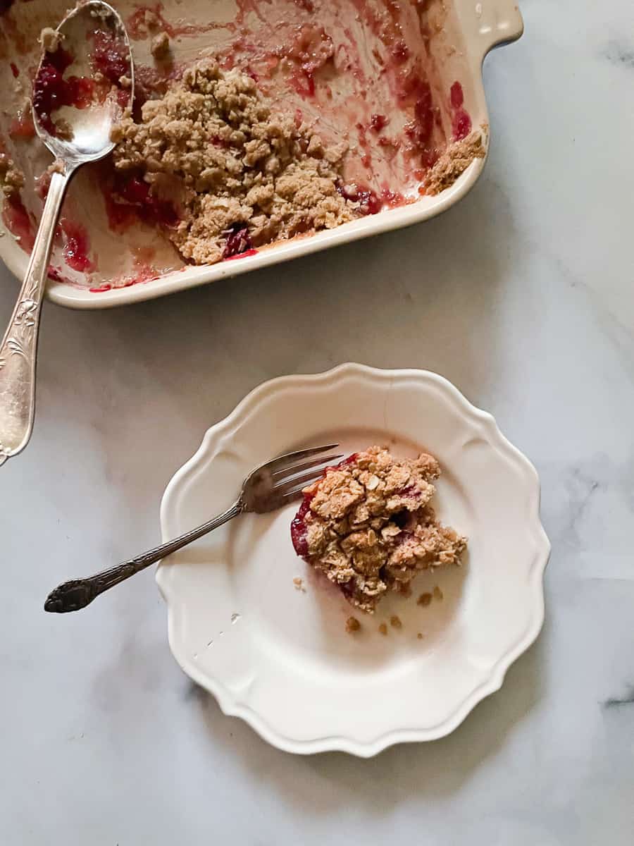 A pan of cranberry apple crisp with a plate of crisp with a fork on a plate.