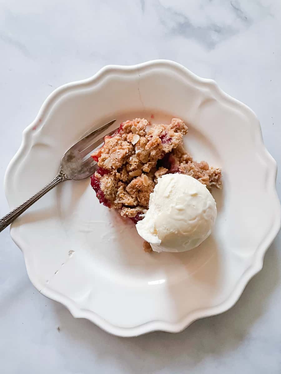 A piece of cranberry apple crisp is shown with a fork on a white plate topped with vanilla ice cream.