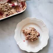 A portion of cranberry apple crisp on a plate next to a pan of crisp.