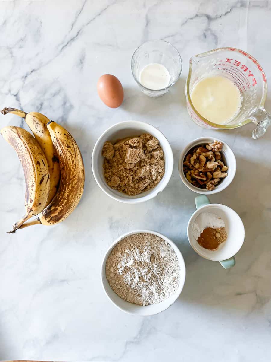 Ingredients for oat flour banana muffins are portioned out: bananas, eggs, oat flour, baking soda, baking powder, cinnamon and ginger, salt, butter, milk.