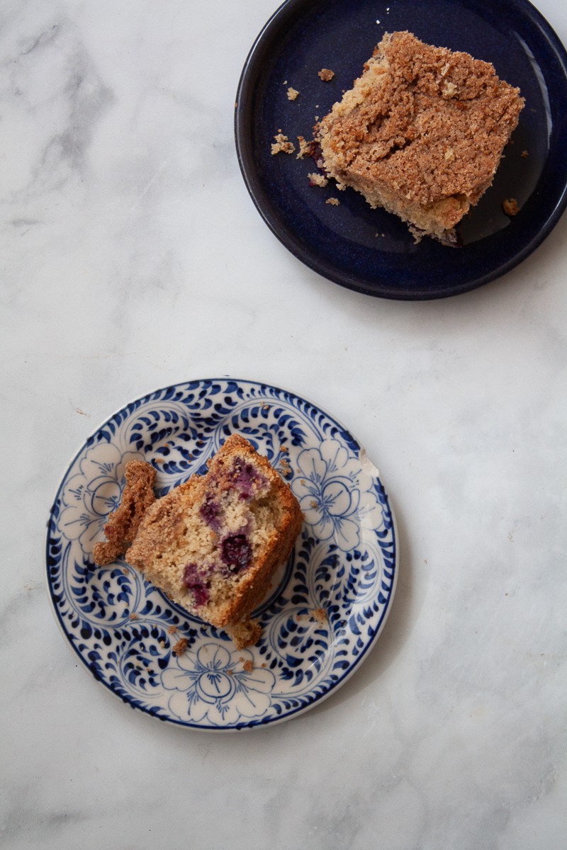 Two pieces of gluten free blueberry coffee cake on plates with one turned on its side