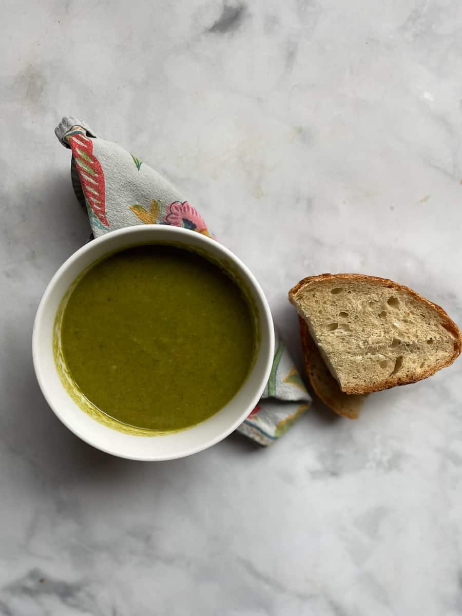 A serving of vegan asparagus soup in a bowl with a slice of bread.