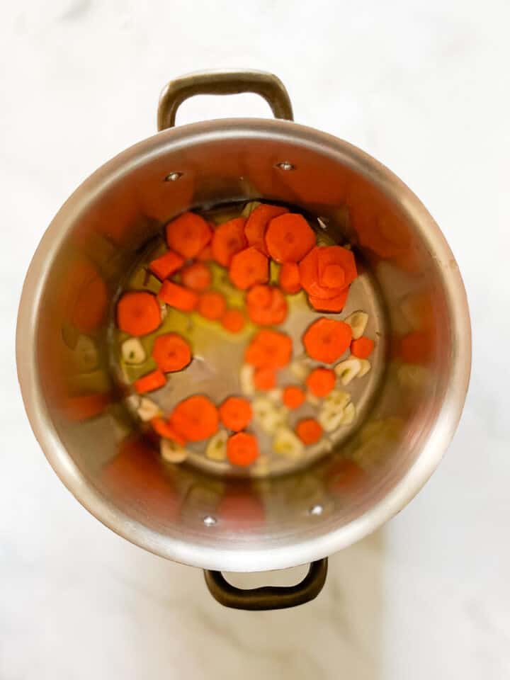 Garlic and carrots sautee in a soup pot.