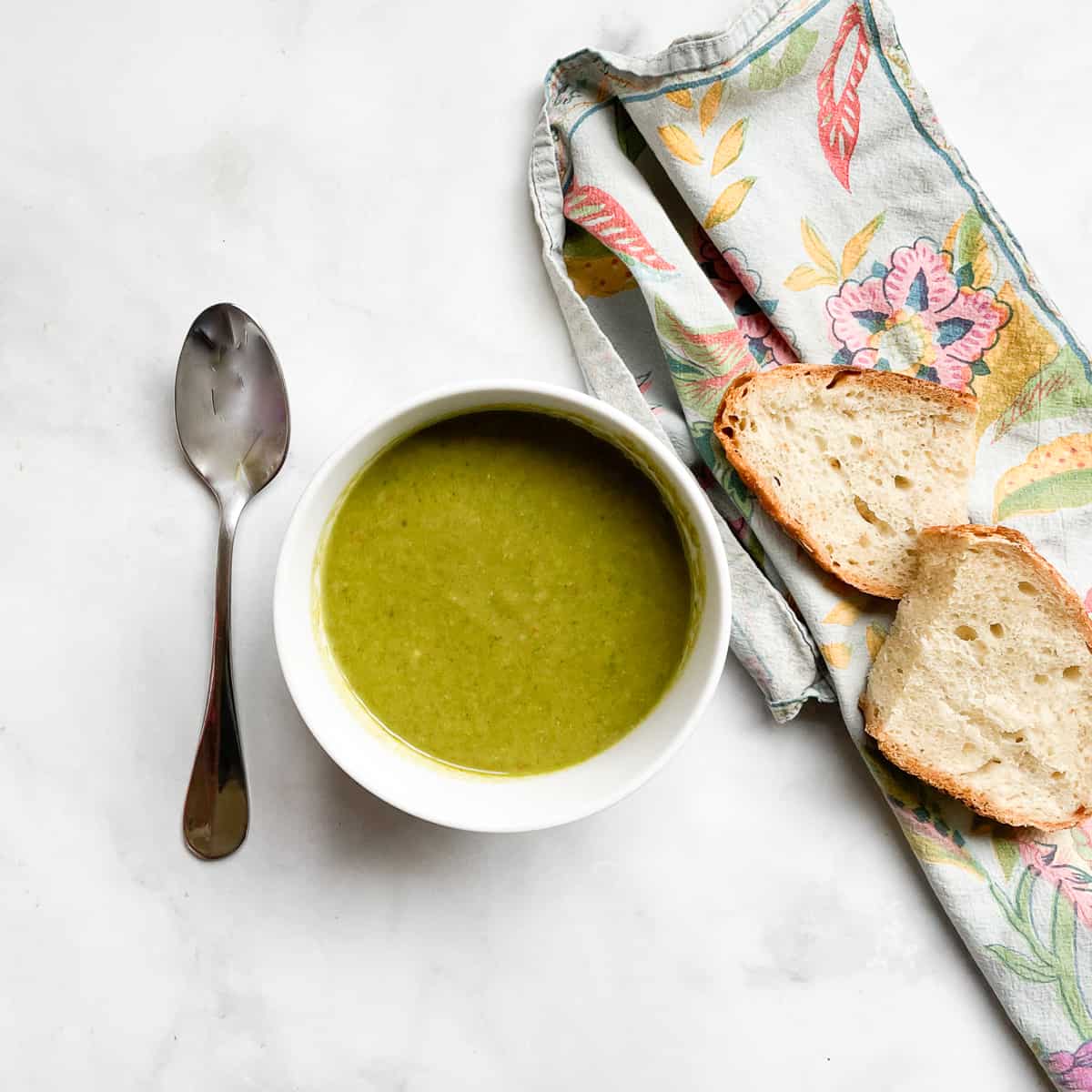 Two slices of bread on a napkin next to a bowl of vegan asparagus soup.