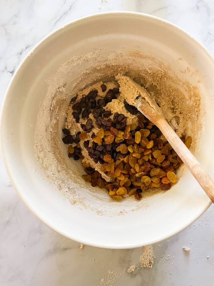 A wooden spoon stirs raisins into the dough.