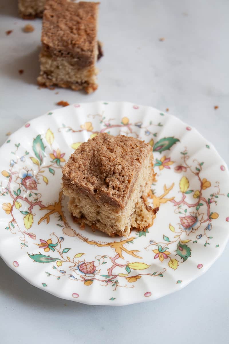 A plate with a piece of gluten free coffee cake with more in the background.